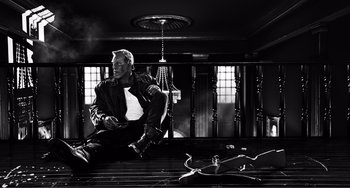Movie still from “Sin City: A Dame to Kill For” (2014), directed by Frank Miller – A black and white photo of a man sitting on a chair; Wide shot, Low angle