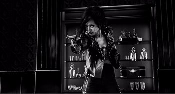 Movie still from “Sin City: A Dame to Kill For” (2014), directed by Frank Miller – A woman holding a gun in a room filled with shelves; Medium shot, Low angle