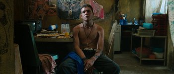 Movie still from “Sin Nombre” (2009), directed by Cary Joji Fukunaga – A young man sitting in a room with his hands on his knees; Medium shot, Low angle