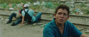 Movie still from “Sin Nombre” (2009), directed by Cary Joji Fukunaga – A man sitting next to a man laying on the ground; Close Up shot, Low angle