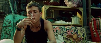 Movie still from “Sin Nombre” (2009), directed by Cary Joji Fukunaga – A man sitting on a couch smoking a cigarette; Close Up shot, High angle