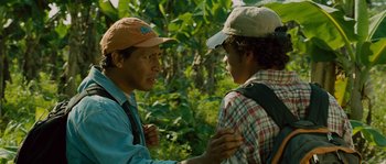 Movie still from “Sin Nombre” (2009), directed by Cary Joji Fukunaga – Two men are talking in the woods near trees; Medium shot, Over the shoulder angle