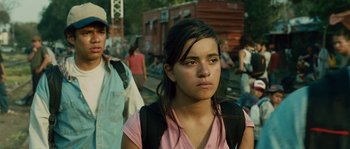 Movie still from “Sin Nombre” (2009), directed by Cary Joji Fukunaga – A young girl is standing in front of a crowd of onlookers; Medium shot, Over the shoulder angle