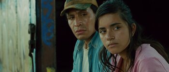 Movie still from “Sin Nombre” (2009), directed by Cary Joji Fukunaga – A man and a woman sitting next to each other in front of a wall; Close Up shot, Low angle