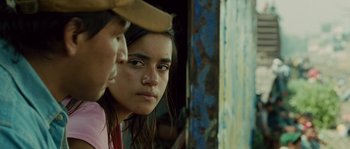 Movie still from “Sin Nombre” (2009), directed by Cary Joji Fukunaga – A young woman looking at the camera while wearing a cowboy hat; Close Up shot, Over the shoulder angle