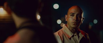 Movie still from “Sin Nombre” (2009), directed by Cary Joji Fukunaga – A man with a shaved head is looking at a microphone; Close Up shot, Over the shoulder angle