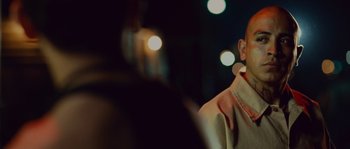 Movie still from “Sin Nombre” (2009), directed by Cary Joji Fukunaga – A person with a microphone in front of some lights; Close Up shot, Over the shoulder angle