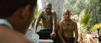 Movie still from “Sin Nombre” (2009), directed by Cary Joji Fukunaga – Two men sitting next to each other with tattoos on their arms; Medium shot, Low angle