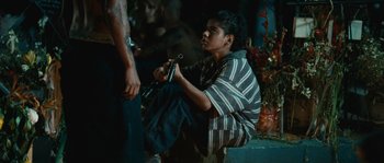 Movie still from “Sin Nombre” (2009), directed by Cary Joji Fukunaga – A man sitting on the ground holding a pipe; Medium shot, Over the shoulder angle