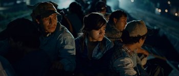 Movie still from “Sin Nombre” (2009), directed by Cary Joji Fukunaga – A group of people sitting in a room at night; Medium shot, High angle