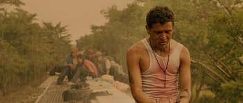 Movie still from “Sin Nombre” (2009), directed by Cary Joji Fukunaga – A man in a pink tank top is sitting in the rain; Medium shot, Low angle