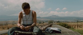Movie still from “Sin Nombre” (2009), directed by Cary Joji Fukunaga – A man sitting on the ground looking at his cell phone; Medium shot, Low angle