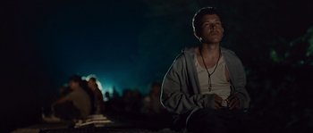 Movie still from “Sin Nombre” (2009), directed by Cary Joji Fukunaga – A man sitting on the ground in front of a group of people; Medium shot, Low angle