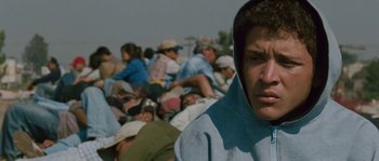 Movie still from “Sin Nombre” (2009), directed by Cary Joji Fukunaga – A man in a hooded sweatshirt is in a crowd of people; Close Up shot, Low angle