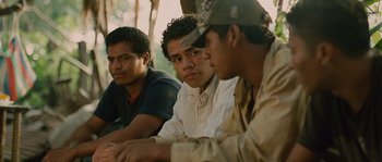Movie still from “Sin Nombre” (2009), directed by Cary Joji Fukunaga – A group of men sitting next to each other on a table; Close Up shot, Over the shoulder angle