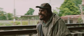 Movie still from “Sin Nombre” (2009), directed by Cary Joji Fukunaga – A man with a beard and a hat is smiling; Medium shot, Low angle