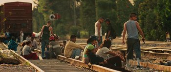 Movie still from “Sin Nombre” (2009), directed by Cary Joji Fukunaga – A group of people sitting on top of a train track; Wide shot, High angle
