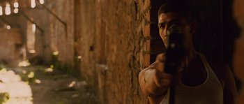 Movie still from “Sin Nombre” (2009), directed by Cary Joji Fukunaga – A man holding a gun while standing next to a brick wall; Medium shot, Over the shoulder angle