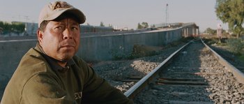 Movie still from “Sin Nombre” (2009), directed by Cary Joji Fukunaga – A man sitting on the side of a train track; Close Up shot, Over the shoulder angle