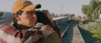 Movie still from “Sin Nombre” (2009), directed by Cary Joji Fukunaga – A man carrying a woman on his back on the side of a train track; Close Up shot, Over the shoulder angle