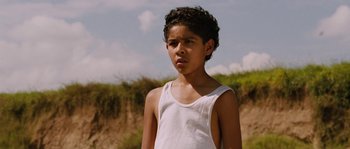 Movie still from “Sin Nombre” (2009), directed by Cary Joji Fukunaga – A young boy wearing a white tank top standing in a field; Close Up shot, Low angle