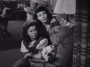Movie still from “Since You Went Away” (1944), directed by John Cromwell – Two young girls sitting in a chair with a dog; Medium shot, High angle