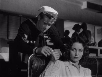 Movie still from “Since You Went Away” (1944), directed by John Cromwell – A man in a sailor's uniform is cutting a woman's hair; Medium shot, Over the shoulder angle