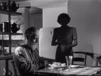 Movie still from “Since You Went Away” (1944), directed by John Cromwell – An older man sitting at a table with a woman standing next to him; Medium shot, Low angle