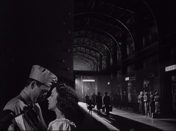 Movie still from “Since You Went Away” (1944), directed by John Cromwell – A man and a woman standing next to each other in a train station; Wide shot, Low angle
