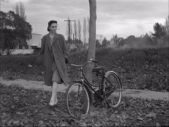 Movie still from “Since You Went Away” (1944), directed by John Cromwell – A woman standing next to a bicycle in a field; Wide shot, High angle