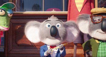Movie still from “Sing” (2016), directed by Christophe Lourdelet – A cartoon koala is holding a pair of scissors in his mouth; Medium shot, Low angle