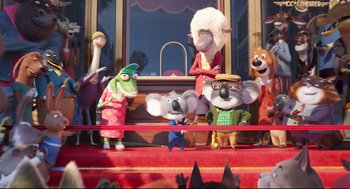Movie still from “Sing” (2016), directed by Christophe Lourdelet – A group of people standing on top of a red stage; Wide shot, High angle