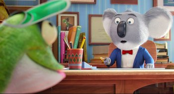 Movie still from “Sing” (2016), directed by Christophe Lourdelet – A koala and a parrot are sitting at a desk; Medium shot, Over the shoulder angle