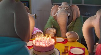 Movie still from “Sing” (2016), directed by Christophe Lourdelet – An elephant sitting at a table in front of a birthday cake; Medium shot, High angle
