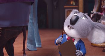 Movie still from “Sing” (2016), directed by Christophe Lourdelet – A white dog wearing a blue suit and holding a pencil; Medium shot, Over the shoulder angle