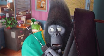 Movie still from “Sing” (2016), directed by Christophe Lourdelet – A stuffed gorilla sitting in a chair holding a remote control; Medium shot, High angle