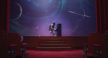 Movie still from “Sing” (2016), directed by Christophe Lourdelet – A person in a suit and helmet playing a piano on a stage; Extreme Wide shot, Low angle