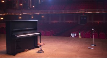 Movie still from “Sing” (2016), directed by Christophe Lourdelet – An empty stage with an upright piano in the middle of the floor; Wide shot, High angle