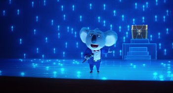 Movie still from “Sing” (2016), directed by Christophe Lourdelet – A small koala is standing on a stage with a microphone in his hand; Wide shot, Low angle