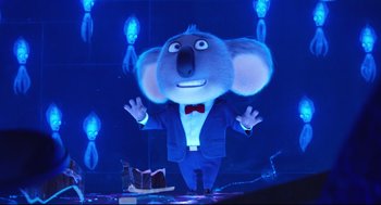 Movie still from “Sing” (2016), directed by Christophe Lourdelet – A character in a suit and bow tie standing in front of a cake; Medium shot, Low angle