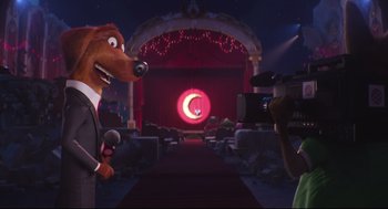 Movie still from “Sing” (2016), directed by Christophe Lourdelet – A person is filming a cartoon character in front of a stage; Wide shot, Over the shoulder angle