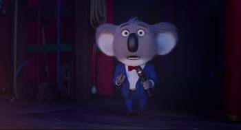 Movie still from “Sing” (2016), directed by Christophe Lourdelet – A koala character holding a microphone in a suit and tie; Medium shot, Low angle