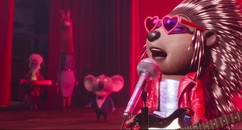 Movie still from “Sing” (2016), directed by Christophe Lourdelet – A person with a microphone and a mouse in the background; Medium shot, Low angle
