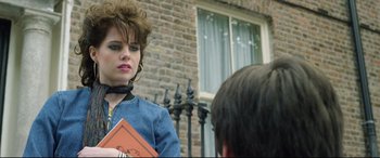 Movie still from “Sing Street” (2016), directed by John Carney – A woman holding a book while standing next to a brick building; Close Up shot, Over the shoulder angle