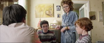 Movie still from “Sing Street” (2016), directed by John Carney – A woman and a boy are standing in a living room; Medium shot, Over the shoulder angle