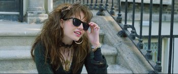 Movie still from “Sing Street” (2016), directed by John Carney – A woman with long brown hair wearing sunglasses and holding her hand up to her face; Medium shot, Over the shoulder angle