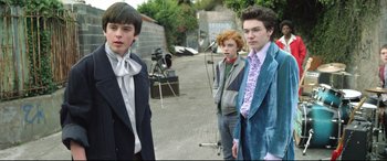 Movie still from “Sing Street” (2016), directed by John Carney – A group of young men standing next to each other on a street; Medium shot, Over the shoulder angle
