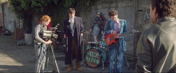 Movie still from “Sing Street” (2016), directed by John Carney – A group of young men standing next to each other on a street; Wide shot, Over the shoulder angle