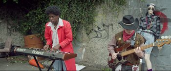 Movie still from “Sing Street” (2016), directed by John Carney – A man in a red jacket playing a keyboard and a man in a brown jacket playing a guitar; Medium shot, Low angle