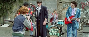 Movie still from “Sing Street” (2016), directed by John Carney – A group of young people standing next to each other on a street; Wide shot, Over the shoulder angle
